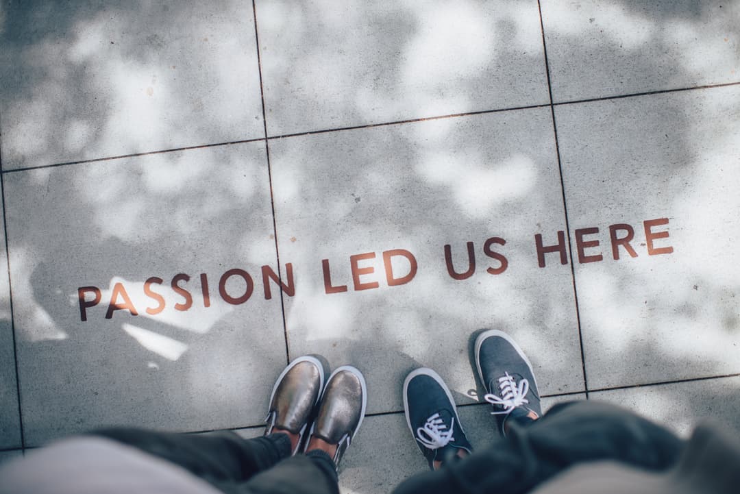 Two peoples feet with text on the floor reading Passion Led Us Here